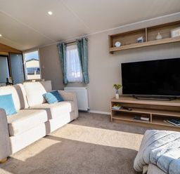 A living room with a beige sofa blue cushions a television on a wooden stand and blue curtains at Wansbeck View 2 in Ashington