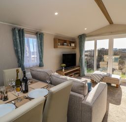 A living and dining area with a dining table set with plates and glasses next to sofas and a television at Wansbeck View 2 in Ashington