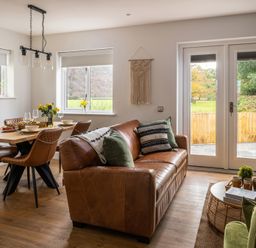 A dining area with a wooden table and brown chairs next to a living room with a brown leather sofa and a round wicker coffee table at Sygun in Beddgelert