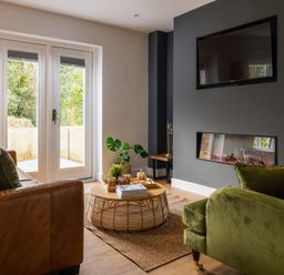 A living room with a brown leather sofa green armchair wooden round coffee table and a wall-mounted television at Sygun in Beddgelert