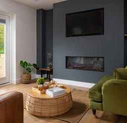 A living room with a green sofa a round wicker coffee table and a built in fireplace at Sygun in Beddgelert