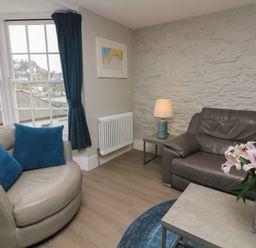 A living room with leather sofas blue cushions a lamp on a side table and flowers on a coffee table at Queens View in Dartmouth