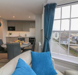 A kitchen and dining area with a round table set for breakfast and a window with blue curtains at Queens View in Dartmouth