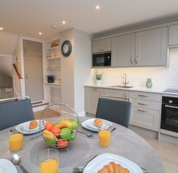A kitchen with gray cabinets, a round dining table set with croissants and orange juice, and a basket of fruit at Queens View in Dartmouth