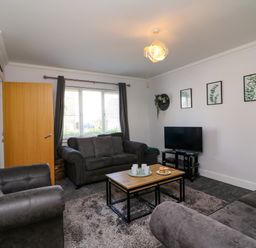 A living room with three gray sofas a wooden coffee table a TV on a stand and framed plant pictures on the wall at Anchors Away in Weymouth