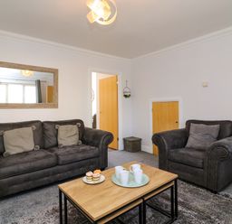 A living room with two dark sofas a wooden coffee table with cups and cupcakes a mirror on the wall and an open door at Anchors Away in Weymouth