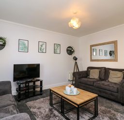 A living room with two sofas a wooden coffee table with cups a TV on a stand and framed botanical prints on the wall at Anchors Away in Weymouth