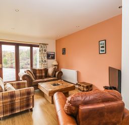 A living room with sofas a wooden coffee table a television and glass doors at The Lodge in Dol-y-Gaer near Pontsticill