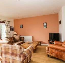 A living room with three armchairs a wooden coffee table a television and a window with curtains at The Lodge in Dol-y-Gaer near Pontsticill