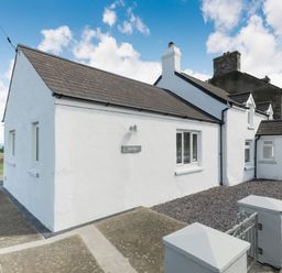 A white cottage with a grey roof and stone chimney under a blue sky at Morlan Cottage in Newport Pembrokeshire