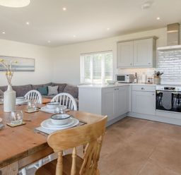 A kitchen and dining area with a wooden table set with dishes and a grey sectional sofa in the corner at Morlan Cottage in Newport Pembrokeshire