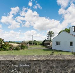 A white cottage with a garden and stone wall under a blue sky with clouds at Morlan Cottage in Newport Pembrokeshire