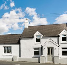 A white cottage with a brown roof and multiple windows under a blue sky at Morlan Cottage in Newport Pembrokeshire
