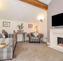 A living room with plaid sofas a fireplace a mounted tv and a small wooden table at Chestnuts Cottage in Windermere