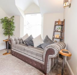A sitting area with a plaid sofa cushions plant small tables and a wooden shelf at Chestnuts Cottage in Windermere