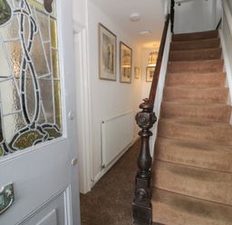 A hallway with a carpeted staircase wooden banister radiator framed pictures and an open door with stained glass at Wenallt in Porthmadog