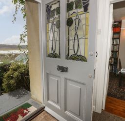 An open front door with stained glass panels looking out to a garden gate and landscape with hills at Wenallt in Porthmadog