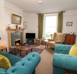 A living room with teal sofas, a fireplace, an armchair, a television, and green curtains at Wenallt in Porthmadog