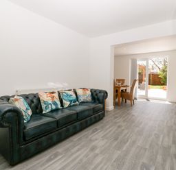 A living room with a black leather sofa and decorative cushions next to a dining area with a wooden table and chairs at Seacider in Burnham-On-Sea