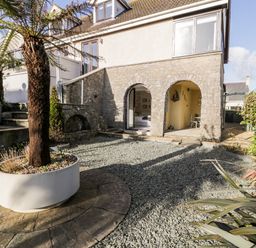 An outside view of a stone house with arched doorways and a garden area with gravel and a tree in a planter at The Chalet in Benllech