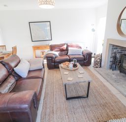 A living room with two brown leather sofas a wooden coffee table a fireplace with firewood and a round mirror on the wall at Little Haven in Bamburgh