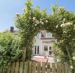 A garden arch with climbing roses over a wooden gate and patio furniture at 3 St Cuthberts Garth in Bamburgh