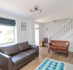 A living room with two leather sofas a staircase and a window at 3 St Cuthberts Garth in Bamburgh