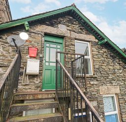 Stone exterior of a building with a green door and metal stairs with railing leading up at Windermere Crescent in Windermere