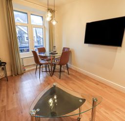 A dining area with a round glass table and four brown chairs a wall mounted TV and a glass coffee table at Windermere Crescent in Windermere