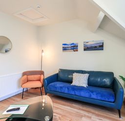 A living room with a blue sofa, an orange armchair, a glass coffee table, wall art, and a plant in a basket at Windermere Crescent in Windermere