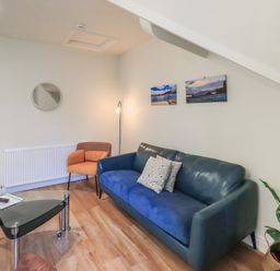 A living room with a blue sofa and orange armchair a glass coffee table and two pictures on the wall at Windermere Crescent in Windermere