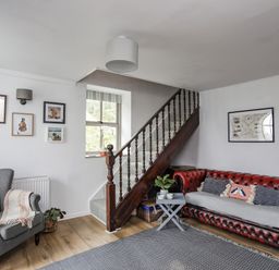 A living room with a red leather sofa, grey armchair, wooden staircase, and wall art at Bethania Llangoed near Beaumaris