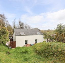 A white house with two skylights and windows surrounded by grassy hills and trees at Bethania in Llangoed near Beaumaris