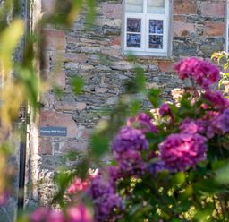 A stone wall house with white windows and pink flowers in the foreground at Cunsey Mill House Cunsey near Hawkshead