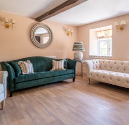 A living room with a green sofa, beige sofa, armchair, round wall mirror, lamps, and wooden floor at Cunsey Mill House Cunsey near Hawkshead
