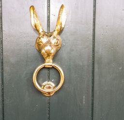 A gold door knocker shaped like a rabbit head on a dark wooden door at The Cheese Room in Stretton-On-Fosse
