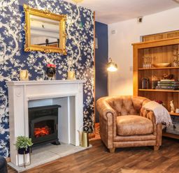 A lounge area with a leather chair a white fireplace and wooden bookshelf at The Cheese Room in Stretton-On-Fosse
