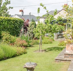 A garden with a variety of plants and flowers a small tree on a lawn a sundial on a pedestal a patio with potted plants a wooden bench and a small garden building with outdoor furniture at Bryn Offa cottage in Holywell