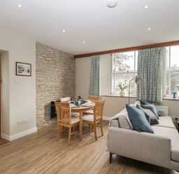 A dining area with wooden table and chairs next to a sofa with cushions by windows at The Old Haberdashery in Swanage