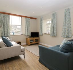 A living room with two sofas a wooden TV stand and windows with patterned curtains at The Old Haberdashery in Swanage