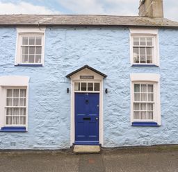 Exterior view of a light blue stone cottage with a blue door and four windows at Bwthyn Dwyfor in Beaumaris