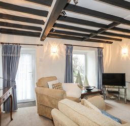 A living room with beige armchairs a glass coffee table and a television at Bwthyn Dwyfor in Beaumaris