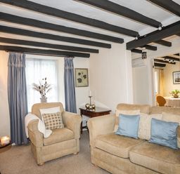 A living room with armchair sofa wooden side tables and blue curtains at Bwthyn Dwyfor in Beaumaris