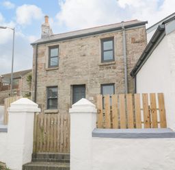 A stone house with wooden gate and white wall on a street corner at Rose Bank Cottage in St Just