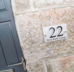 A stone wall with a sign displaying number 22 and Rose Bank Cottage next to a grey door at Rose Bank Cottage in St Just