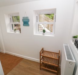 A hallway with three windows a wooden shoe rack a radiator and decorative signs at Rose Bank Cottage St Just