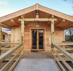 A wooden cabin with a porch and railing at Buttercup Lodge in Theberton near Leiston