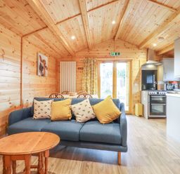 A living room with a blue sofa and wooden table next to a kitchen area at Buttercup Lodge in Theberton near Leiston