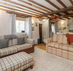 A living room with two patterned sofas a footstool and wooden ceiling beams at Fox Den Cottage in Castle Combe