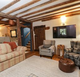 A living room with sofas armchairs a wall mounted TV and exposed wooden beams at Fox Den Cottage in Castle Combe